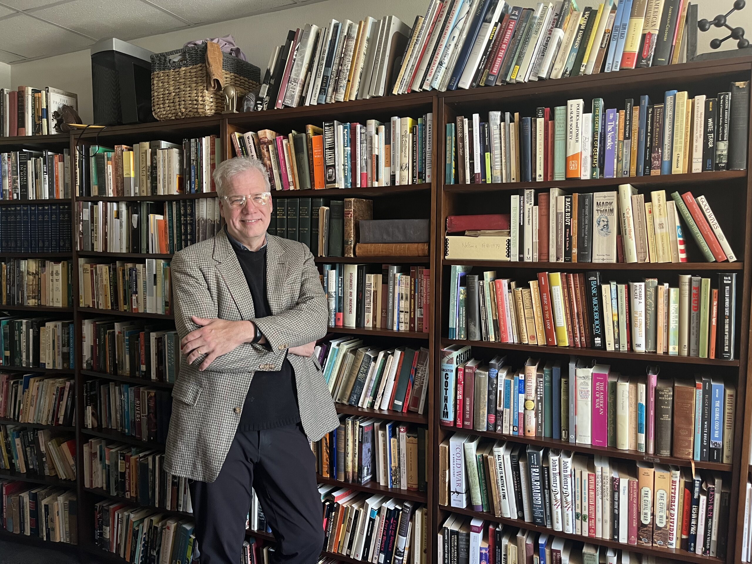 Scott Reynolds Nelson stands with his arms crosse in front of a large bookcase in his office