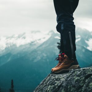 a photo of a hiker's feet wearing brown boots standing on the edge of a rock on a cliff