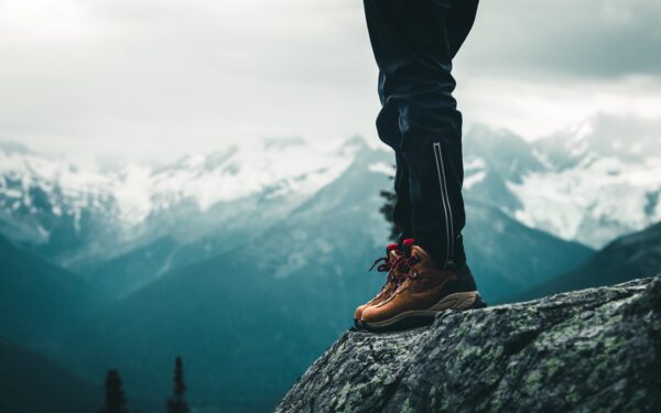 a photo of a hiker's feet wearing brown boots standing on the edge of a rock on a cliff