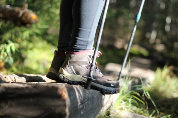 a close-up of a hiker's feet wearing brown boots standing on the edge of a log in the woods