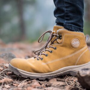 a close-up photo of a hiker's feet wearing brown boots standing on leaves and rocks