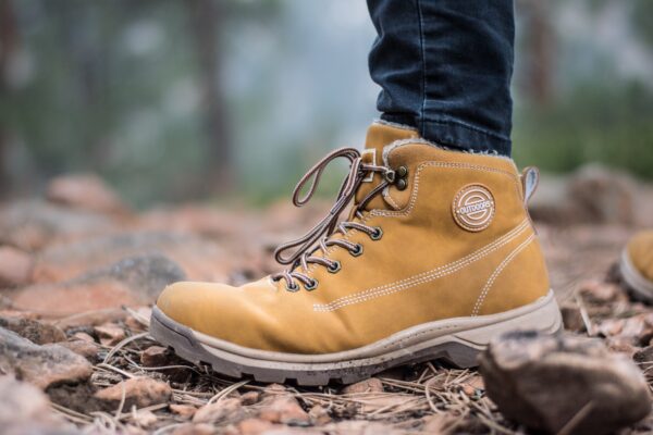 a close-up photo of a hiker's feet wearing brown boots standing on leaves and rocks