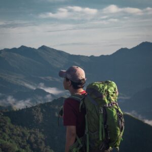 a photo of a hiker wearing a backpack looking off of a summit out into a valley