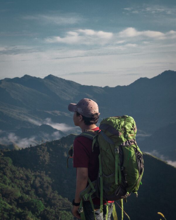 a photo of a hiker wearing a backpack looking off of a summit out into a valley