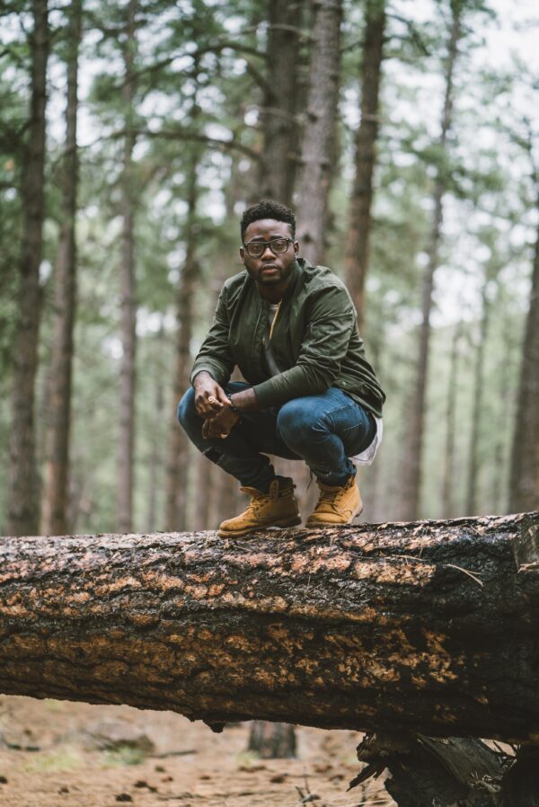 a photo of a man crouching down on a large fallen tree trunk in the woods