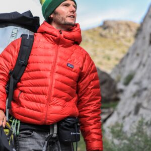 a photo of a hiker in a bright red jacket walking next to a large cliff