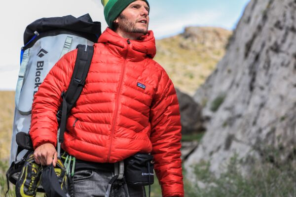 a photo of a hiker in a bright red jacket walking next to a large cliff