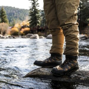 a photo of a hiker modeling hiking boots while standing on a rock in a running creek