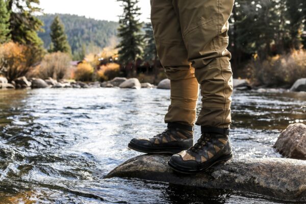 a photo of a hiker modeling hiking boots while standing on a rock in a running creek