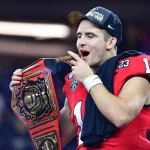 Stetson Bennett holds a championship belt and smokes a cigar on the field after winning the 2023 College Football National Championship