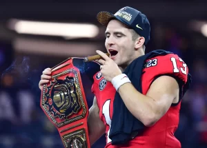 Stetson Bennett holds a championship belt and smokes a cigar on the field after winning the 2023 College Football National Championship